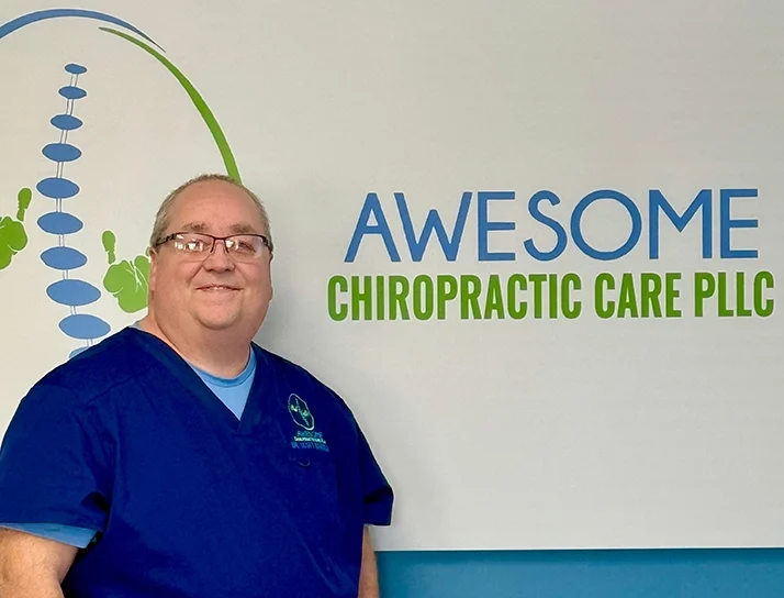 Dr. Scott Renshaw smiling in front of the Awesome Chiropractic Care logo.